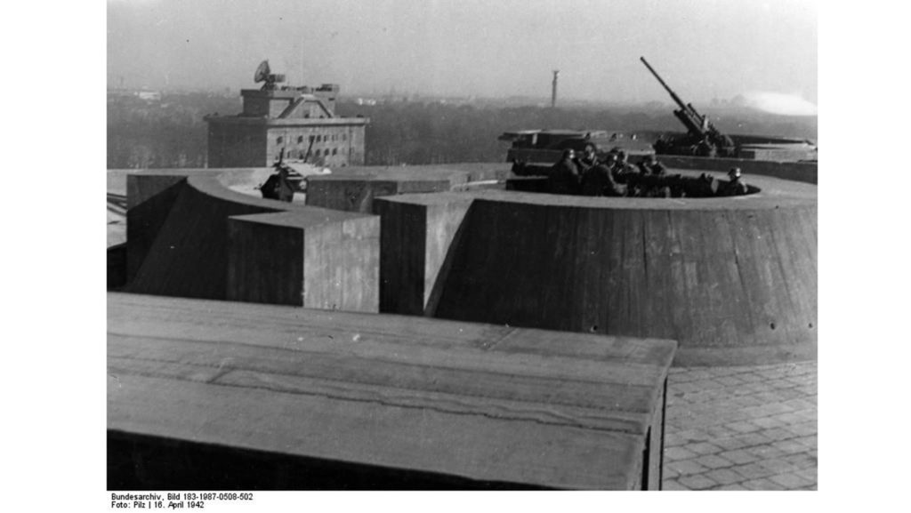 Auf dem Dach des Zoo-Flakturms ist ein Entfernungsmesser (vorne) und ein Flak-Geschütz (hinten) zu sehen. Im Hintergrund steht der Leitturm.