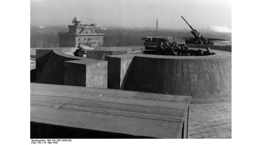 Auf dem Dach des Zoo-Flakturms ist ein Entfernungsmesser (vorne) und ein Flak-Geschütz (hinten) zu sehen. Im Hintergrund steht der Leitturm. 